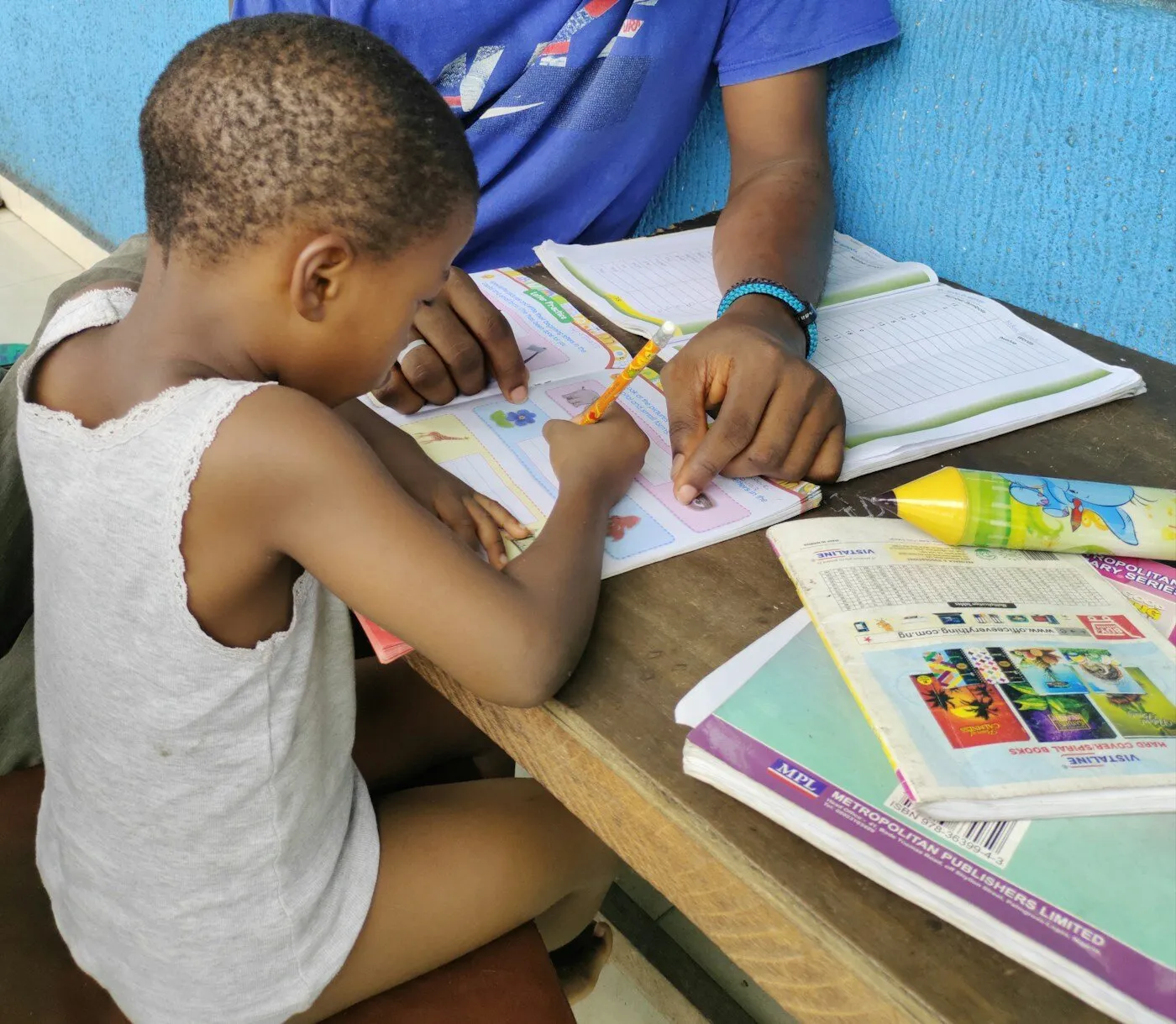 African boy sitting at a table with a book and pencil
