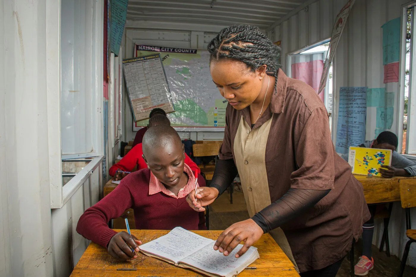 African teacher assisting a student at a desk in a classroom