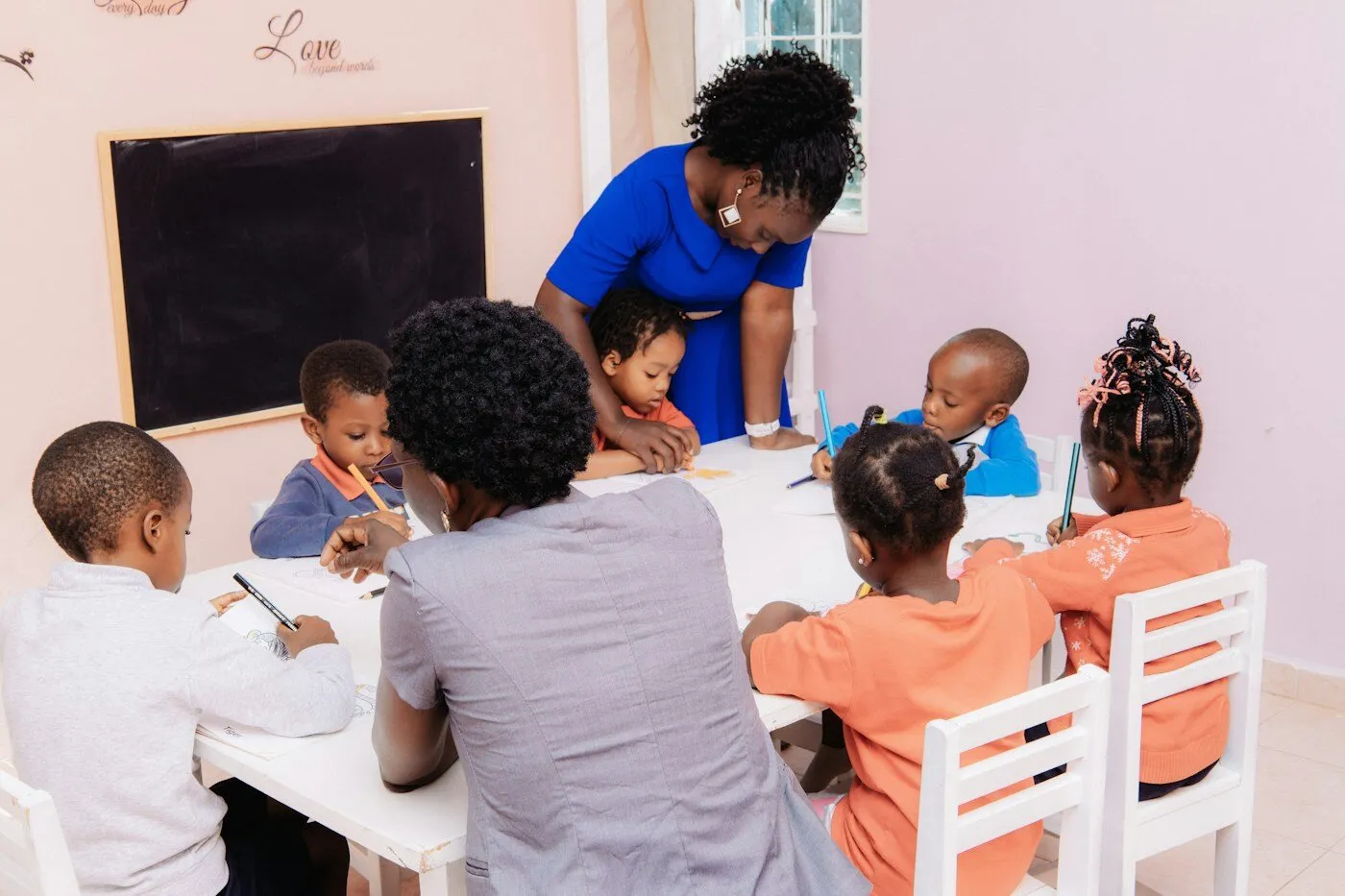 African teacher guiding children drawing at a table