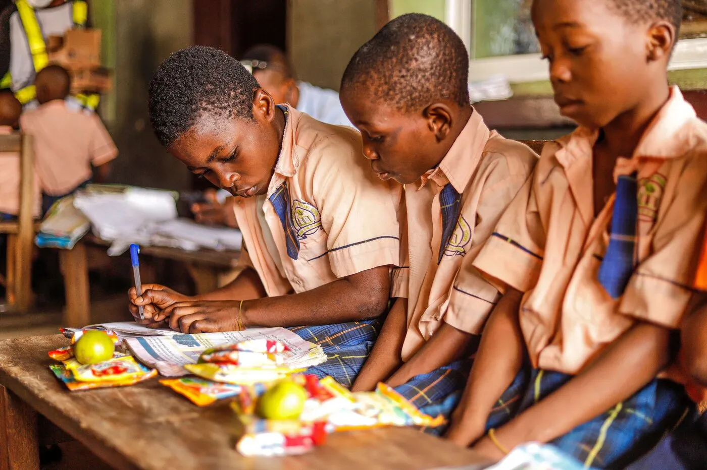 A Kenyan student writing in an exercise book in a classroom